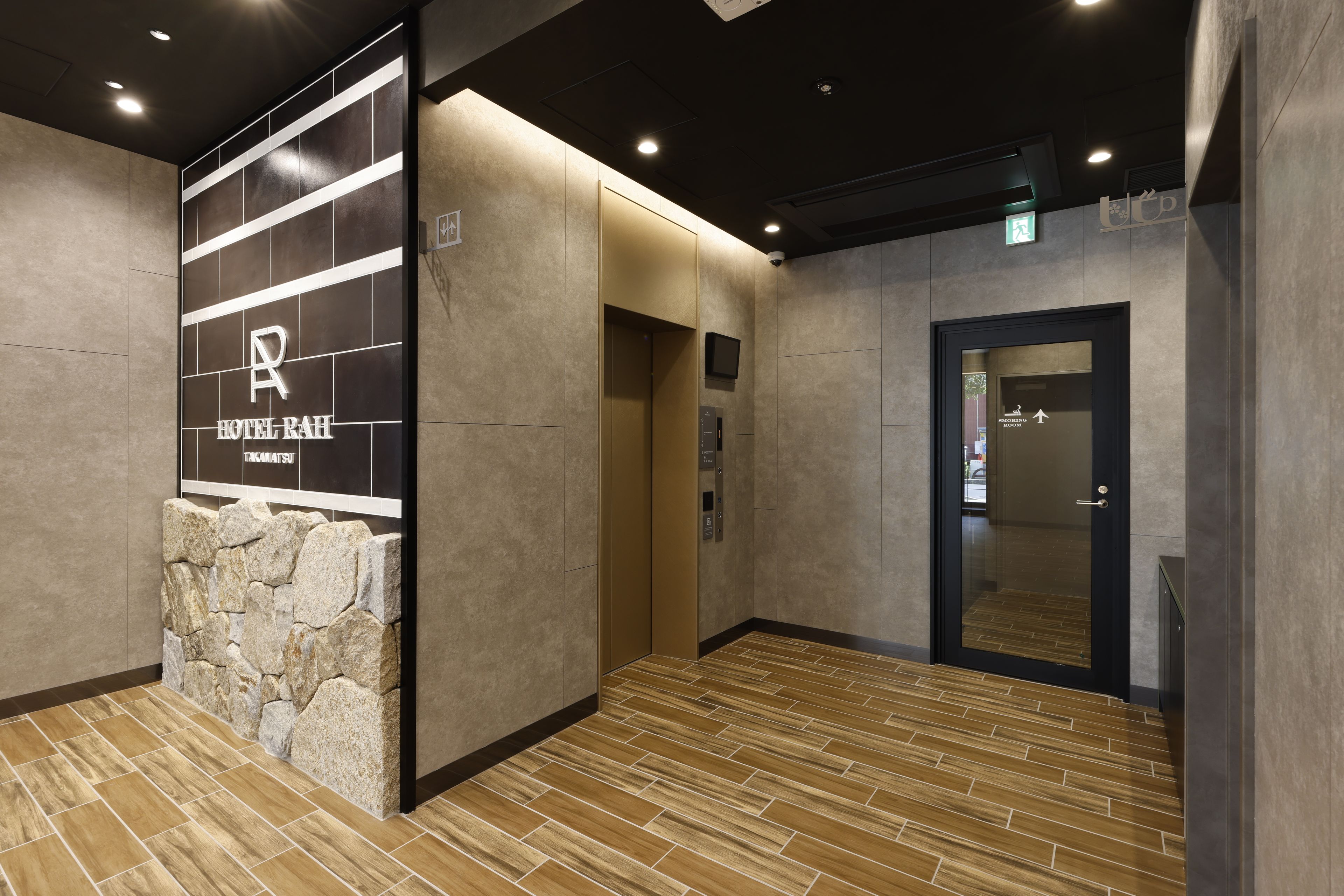 Et hotellobby med en stenvæg, en elevator og en dør med teksten 'Smoking Room'.