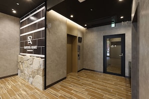 A hotel lobby with a stone wall, an elevator, and a door marked 'Smoking Room'.