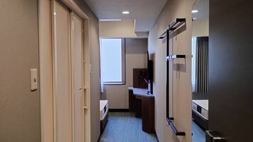 A hotel hallway with a bed, a desk, and a mirror.