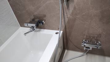 Un baño con una bañera blanca, ducha con cabezal de ducha manual y grifo empotrado en la pared.