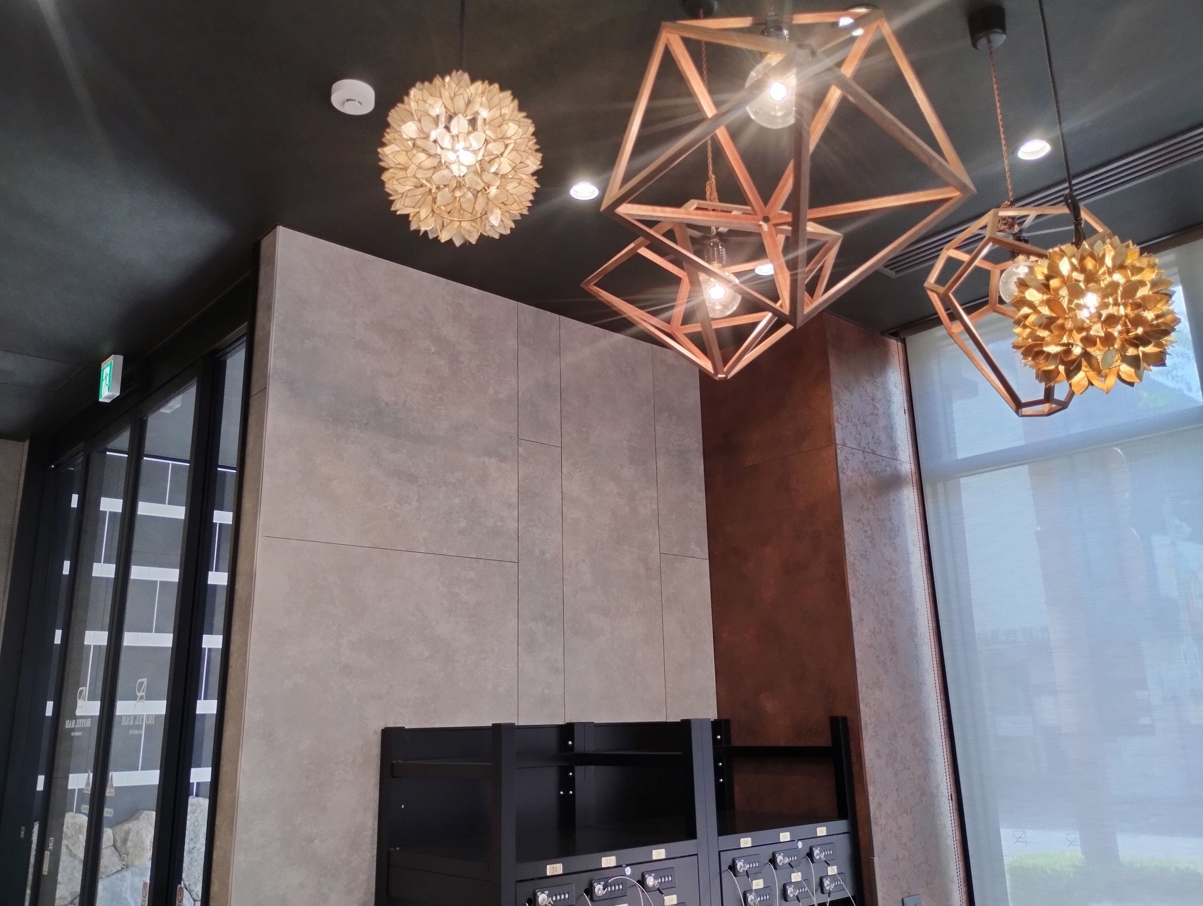 Een modern interieur met een groot raam, een bedieningspaneel aan de muur en geometrische hanglampen.