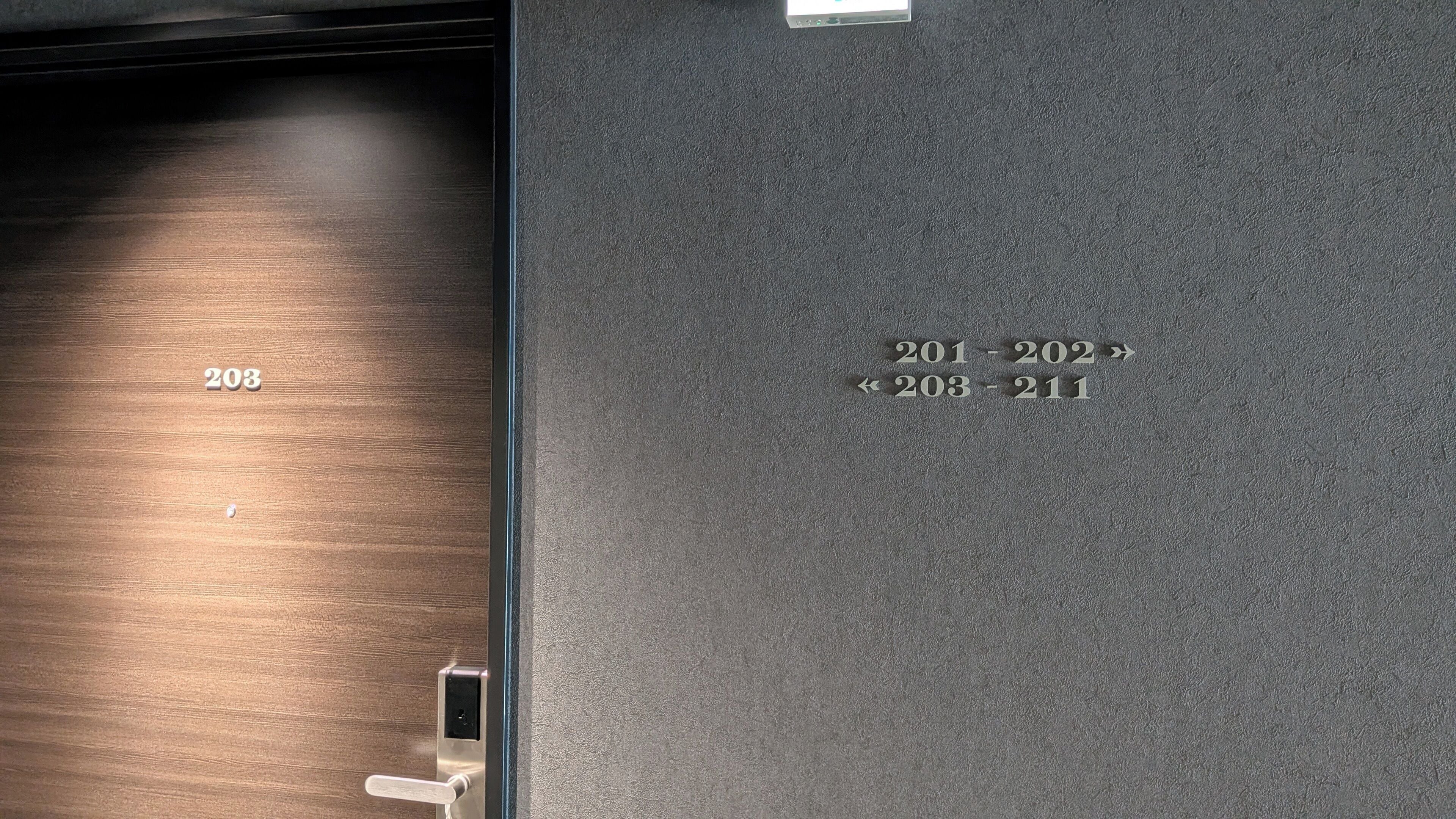 A hotel room with a wooden floor and a door with a metal handle. Room numbers 201-202 and 203-211 are visible.