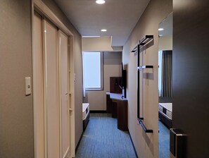 A hotel hallway with a bed, a desk, and a mirror.