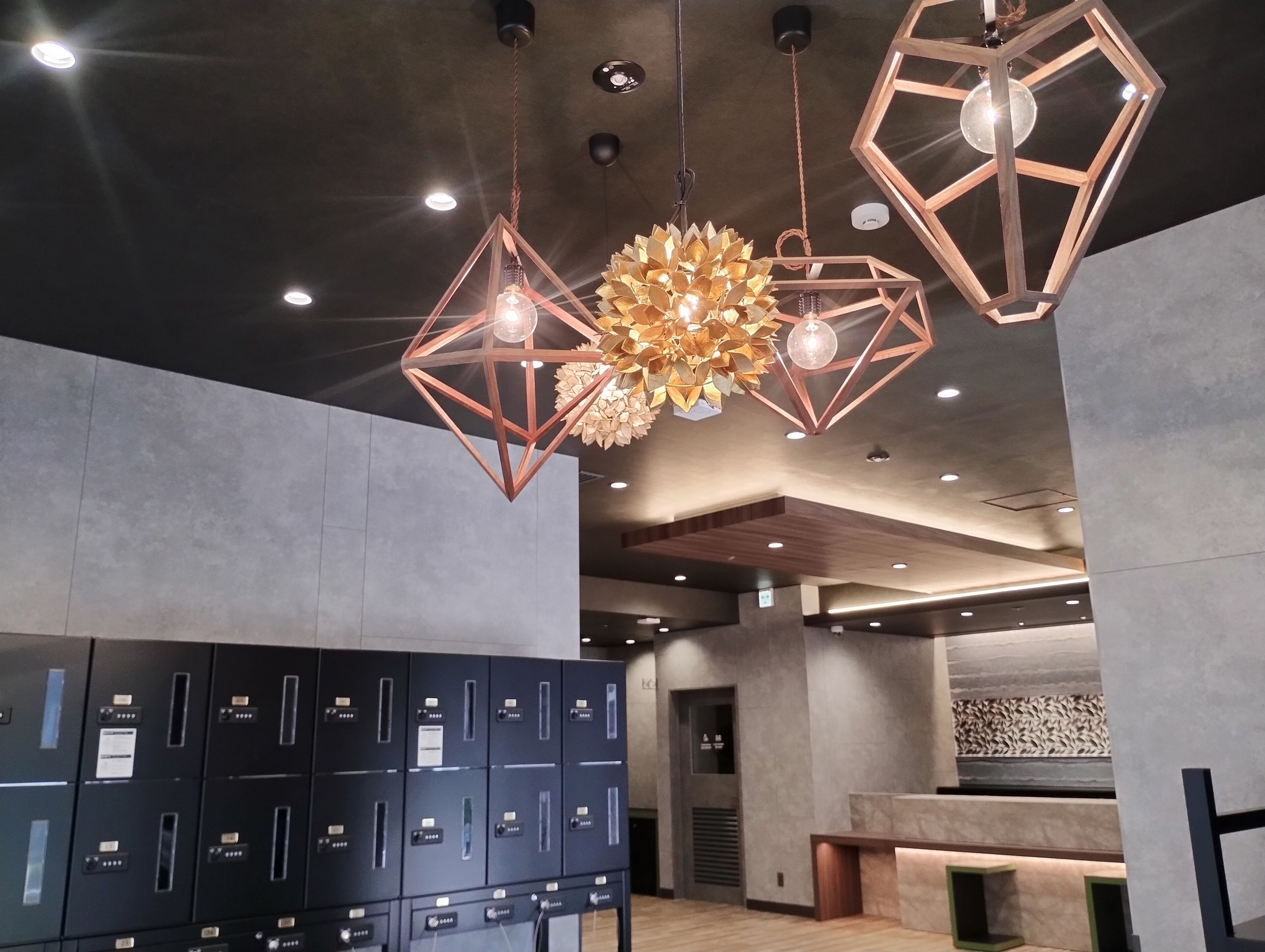 Un interior moderno con lámparas colgantes geométricas, una recepción y una fila de casilleros.