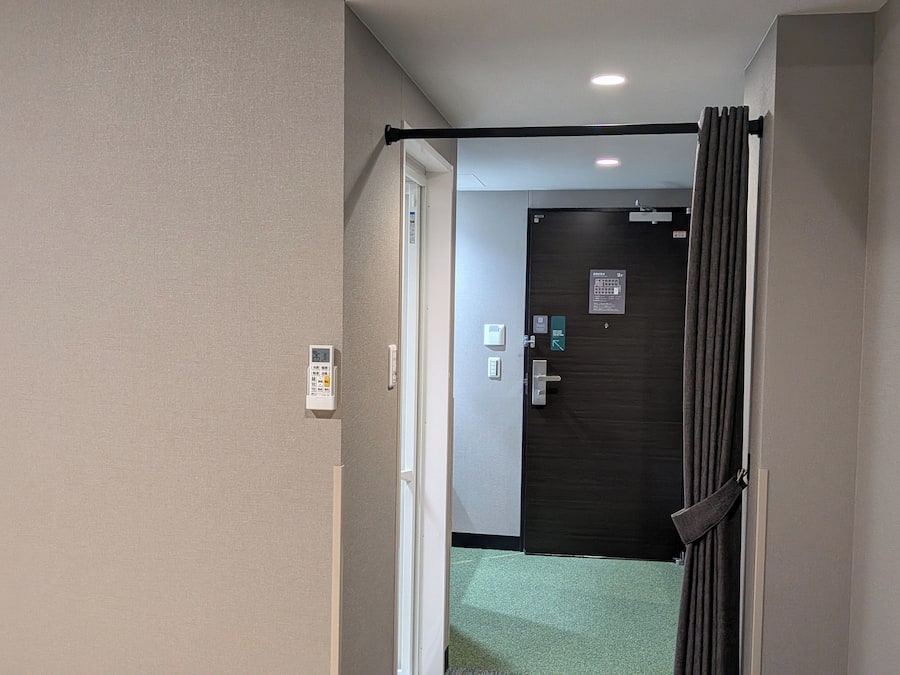 Un couloir avec une porte donnant sur une pièce, un thermostat et un interrupteur.