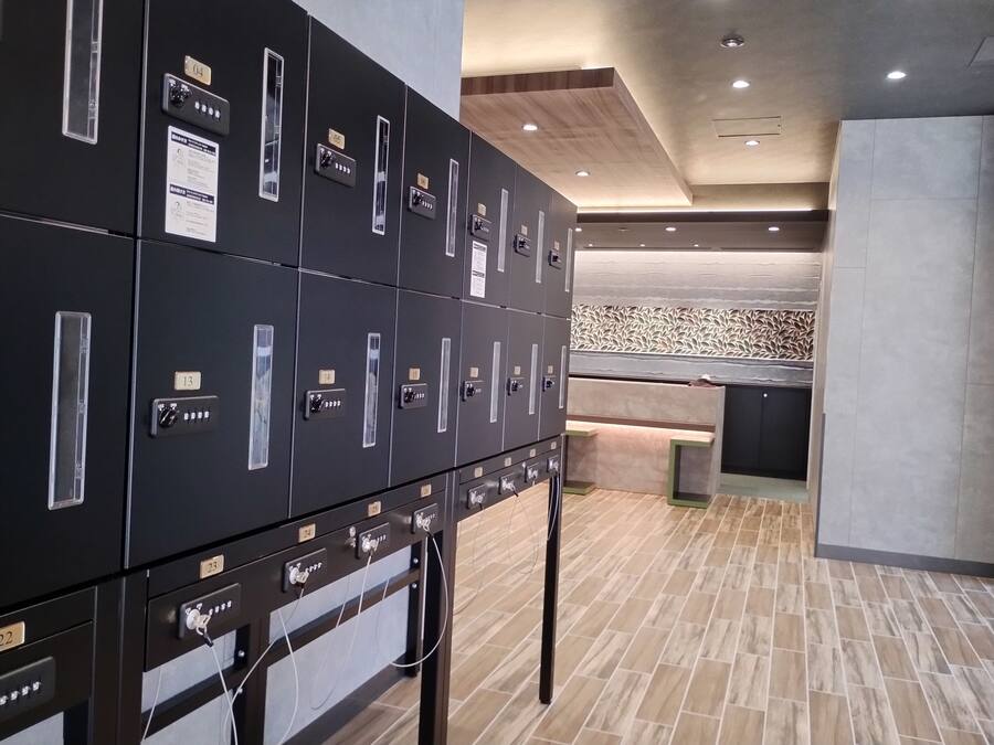 A row of black lockers with numbered labels, a wooden ceiling with recessed lighting, and a patterned wall in the background.