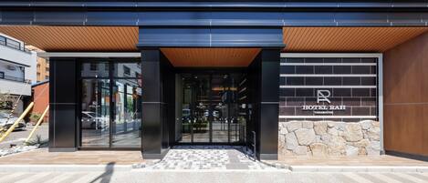 A modern hotel entrance with a glass door, a wooden overhang, and a stone wall.