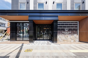 A modern hotel entrance with a glass door, a wooden overhang, and a stone wall. - HOTEL RAH TAKAMATSU (Takamatsu)