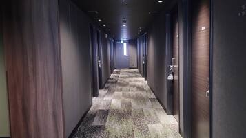 A hotel corridor with a carpeted floor, doors on both sides, and a ceiling with recessed lighting.