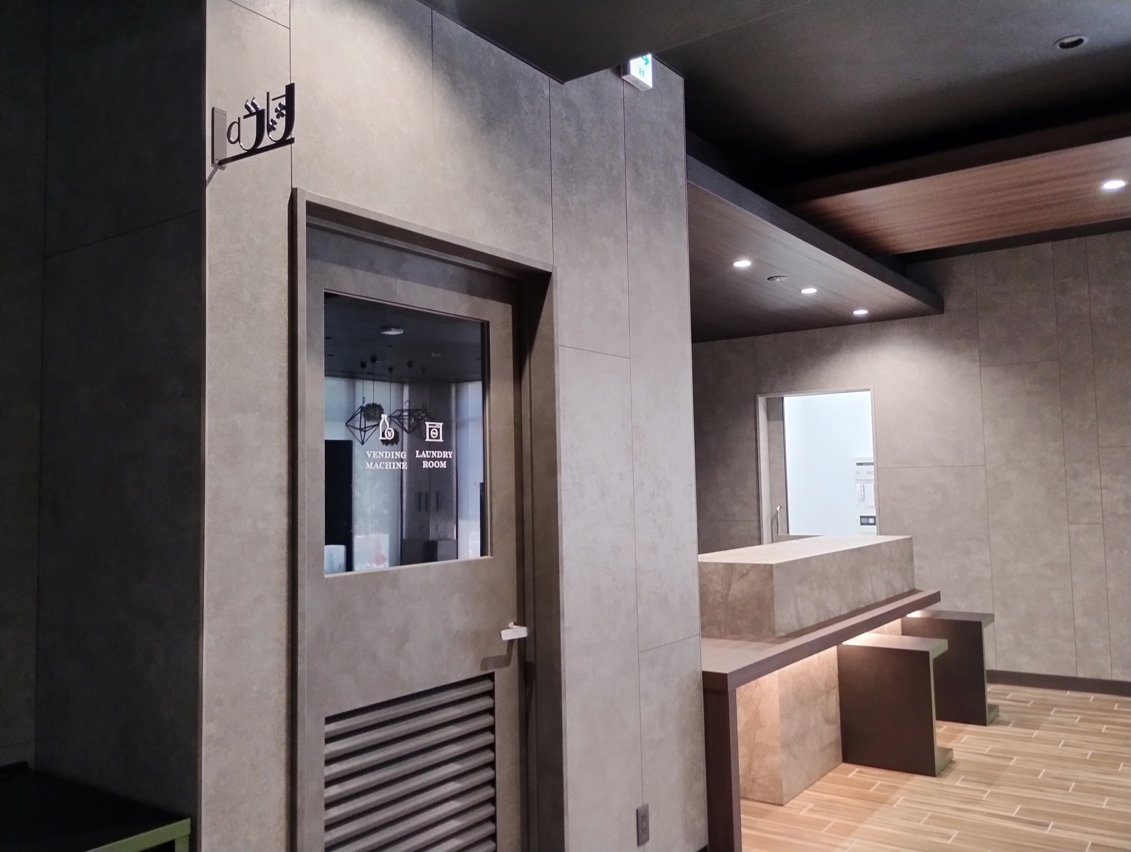 A modern interior with a vending machine and laundry room sign, a reception desk, and a wooden floor.