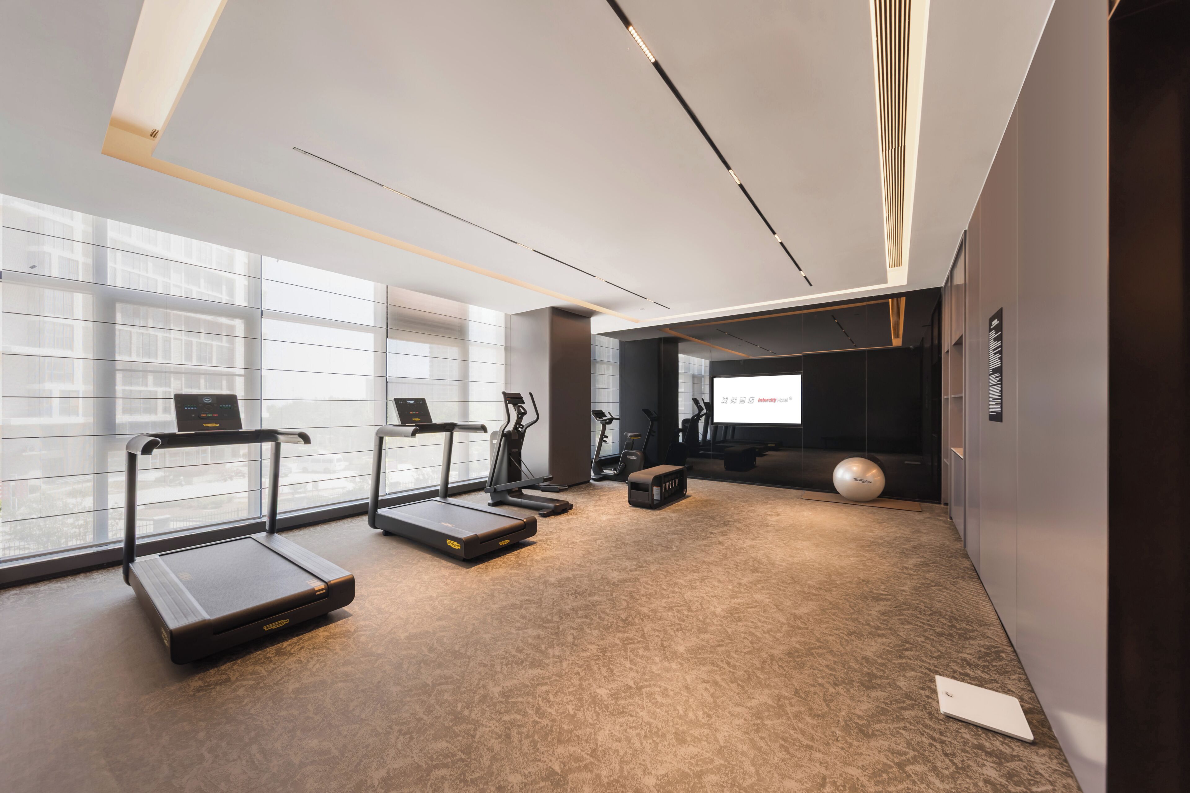 Une salle de sport moderne équipée de tapis de course, de vélos d’appartement et d’un grand écran.