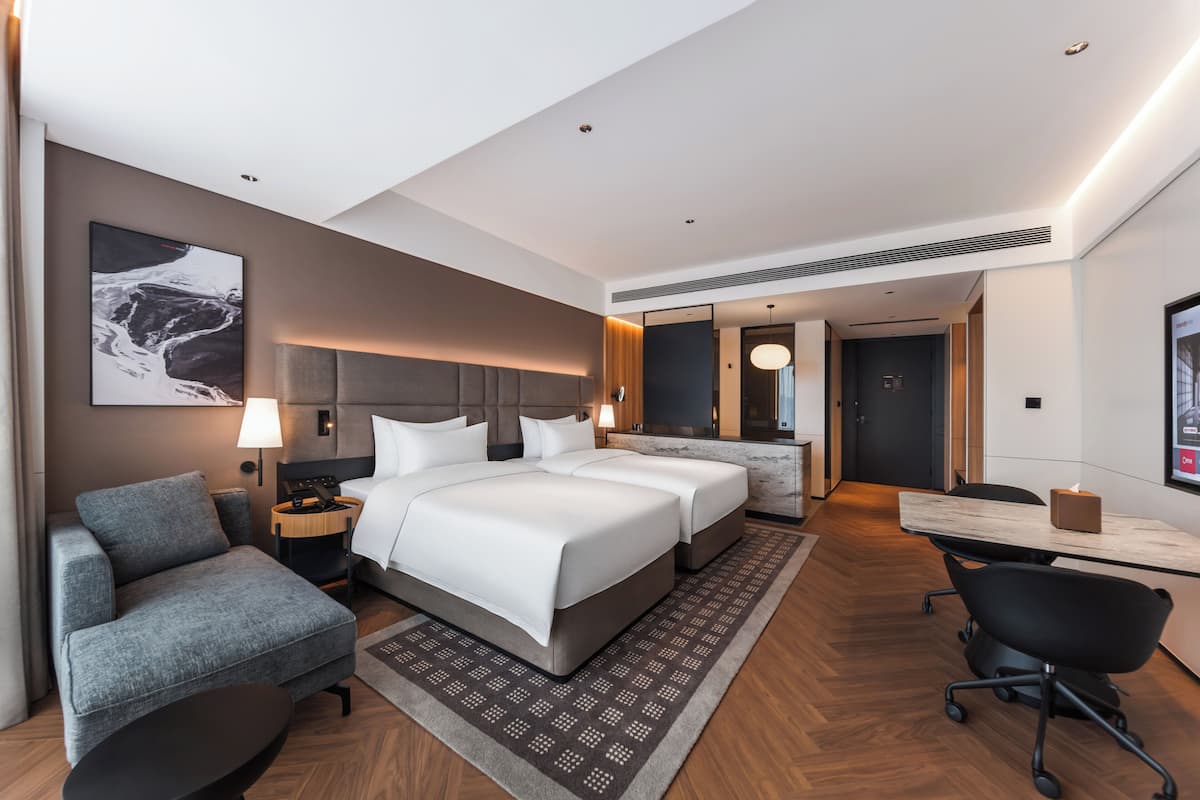 A modern hotel room with a large bed, a desk, a chair, and a sofa.