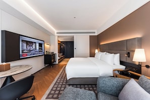 Quarto de hotel com cama, escrivaninha, televisão, sofá e abajur.