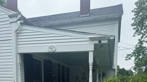 A white house with a porch, a fenced yard, and a chimney. - Step Back in Time, Relax in Modern Comfort (Camden)