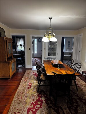 A dining room with a wooden table, chairs, a chandelier, and a patterned rug.
