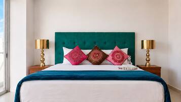 Een bed met een blauwgroen hoofdeinde, witte beddengoed en decoratieve kussens. Er staan twee nachtkastjes met lampen.