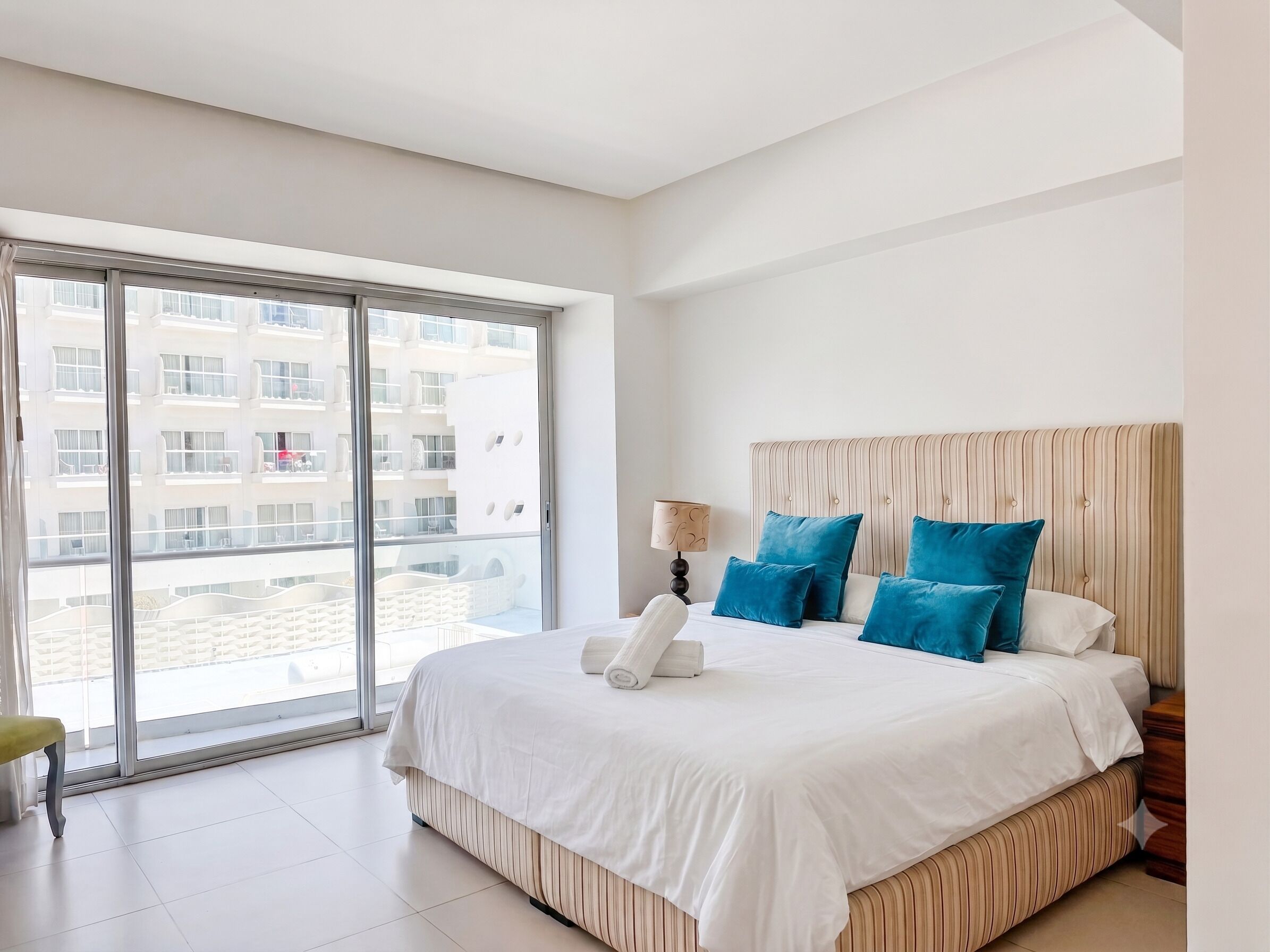 Une chambre d’hôtel avec un grand lit, une fenêtre donnant sur d’autres immeubles et une tête de lit en bois.