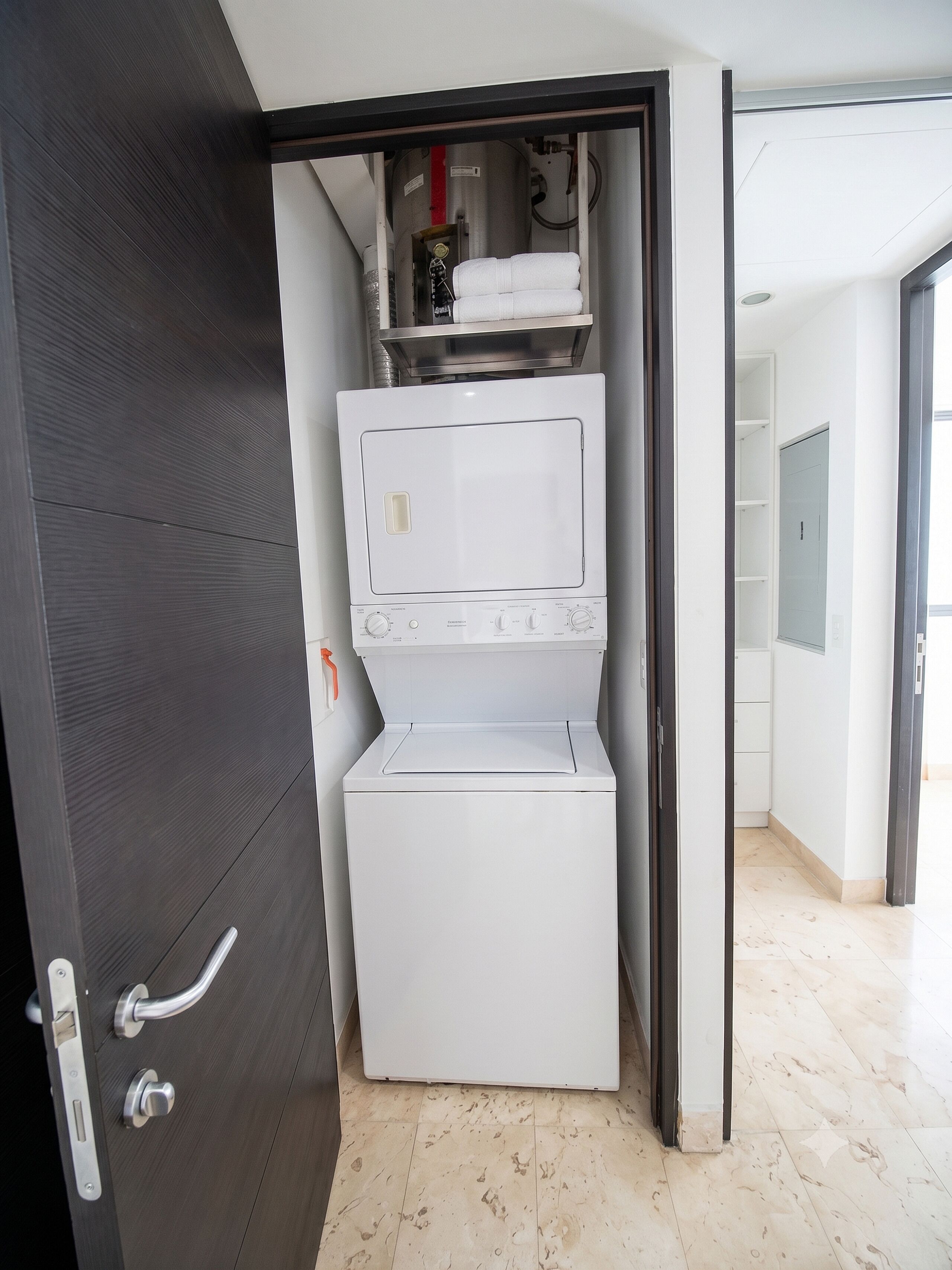 A compact laundry room with a washer and dryer, a metal shelf above the dryer, and a door with a handle.