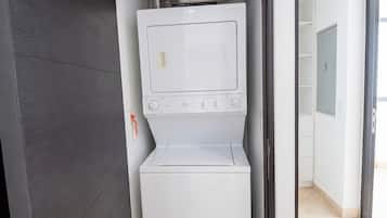 A compact laundry room with a washer and dryer, a metal shelf above the dryer, and a door with a handle.