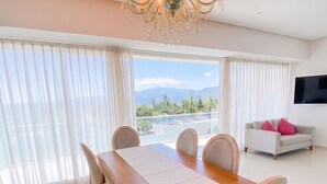A dining area with a wooden table, chairs, a chandelier, a sofa, and a TV. - ICON Oceanview Retreat by Monyxbnb (Puerto Vallarta)
