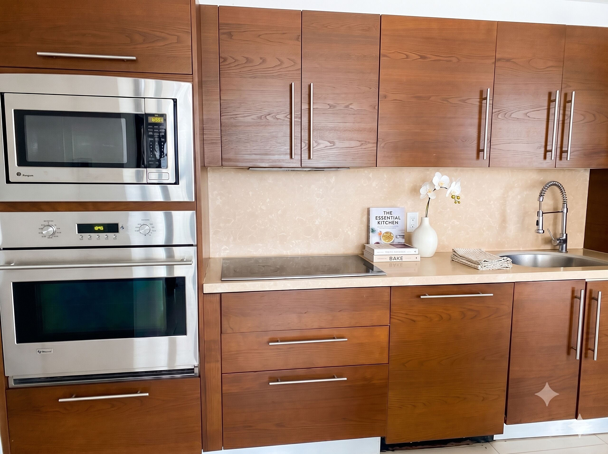 A kitchen with stainless steel appliances, wooden cabinets, a sink, and a vase with flowers.
