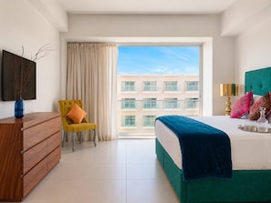 A modern hotel room with a large bed, a wooden dresser, a yellow armchair, and a view of a building through a large window. - ICON Oceanview Retreat by Monyxbnb (Puerto Vallarta)