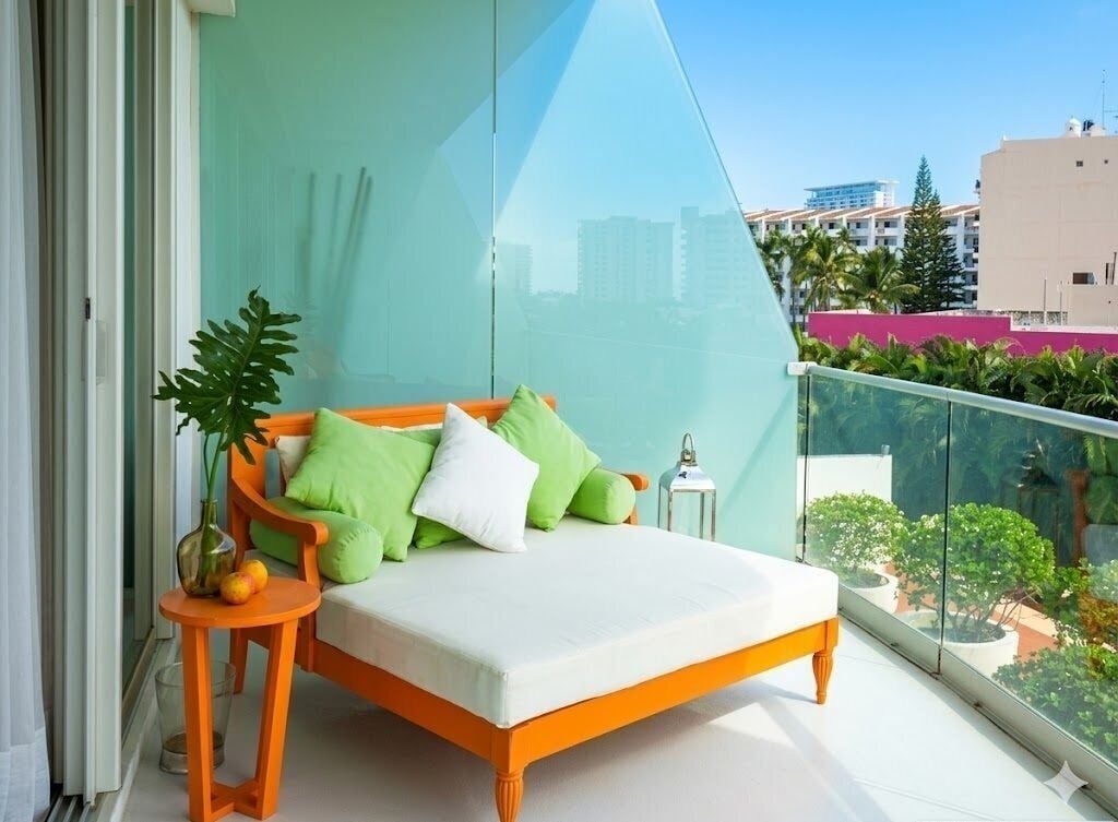 Un balcón con una cama, una planta en maceta y una pequeña mesa con fruta.