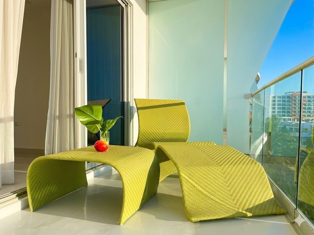 Un balcón con una silla amarilla, una planta en maceta y vistas a edificios.