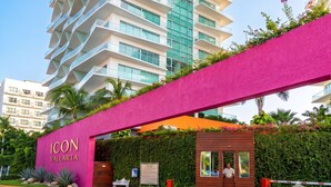 A modern hotel entrance with a prominent pink archway, a wooden bench, and a security gate. - ICON Oceanview Retreat by Monyxbnb (Puerto Vallarta)