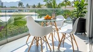 A balcony with a glass table, white chairs, a potted plant, and a view of palm trees and mountains. - ICON Oceanview Retreat by Monyxbnb (Puerto Vallarta)