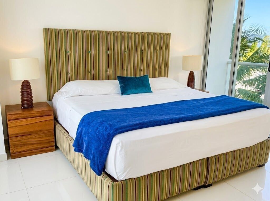 A bed with a striped headboard, white bedding, a blue throw blanket, and two bedside lamps.