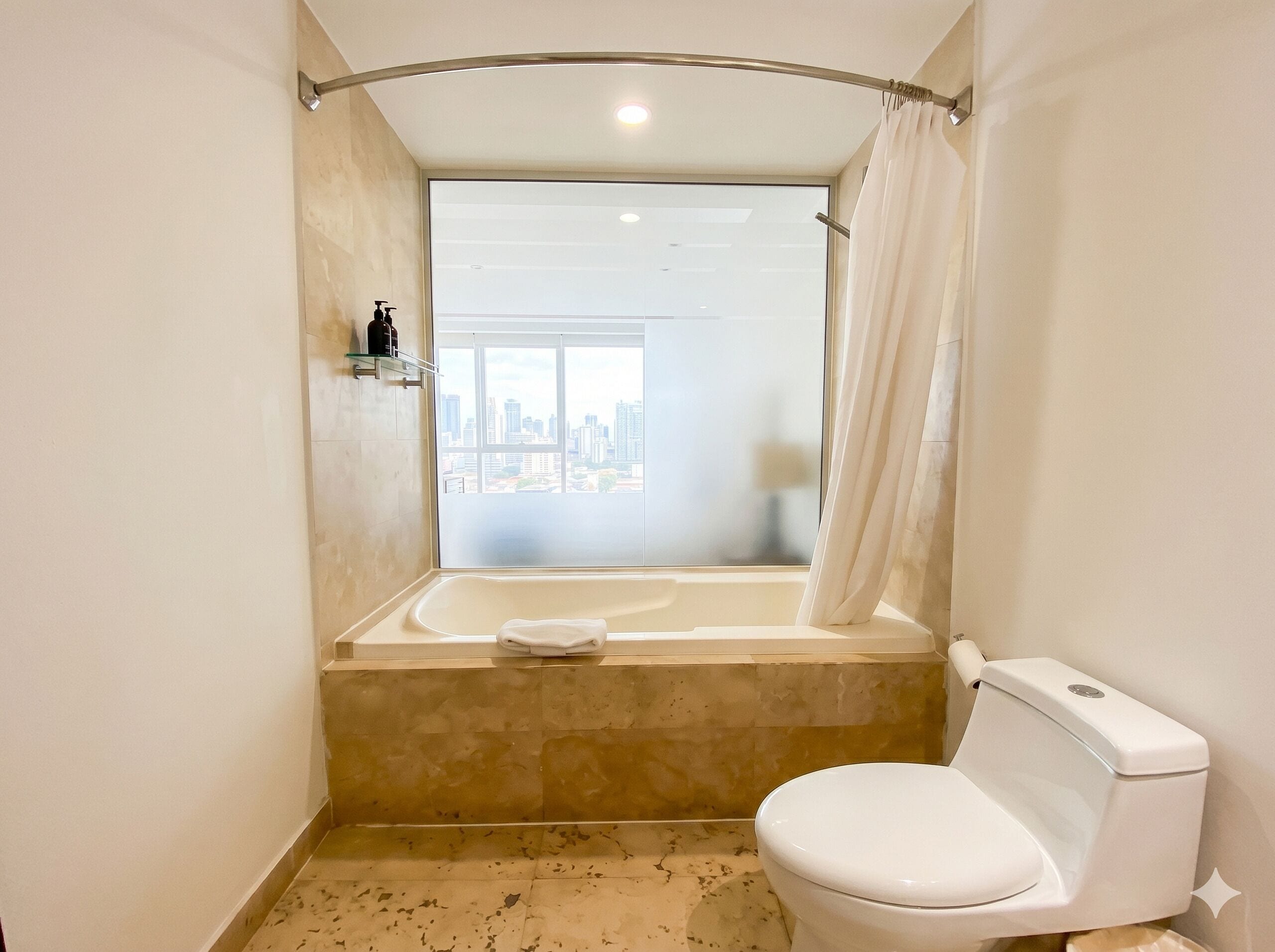 Een badkamer met een bad, toilet en een raam met uitzicht over de stad.