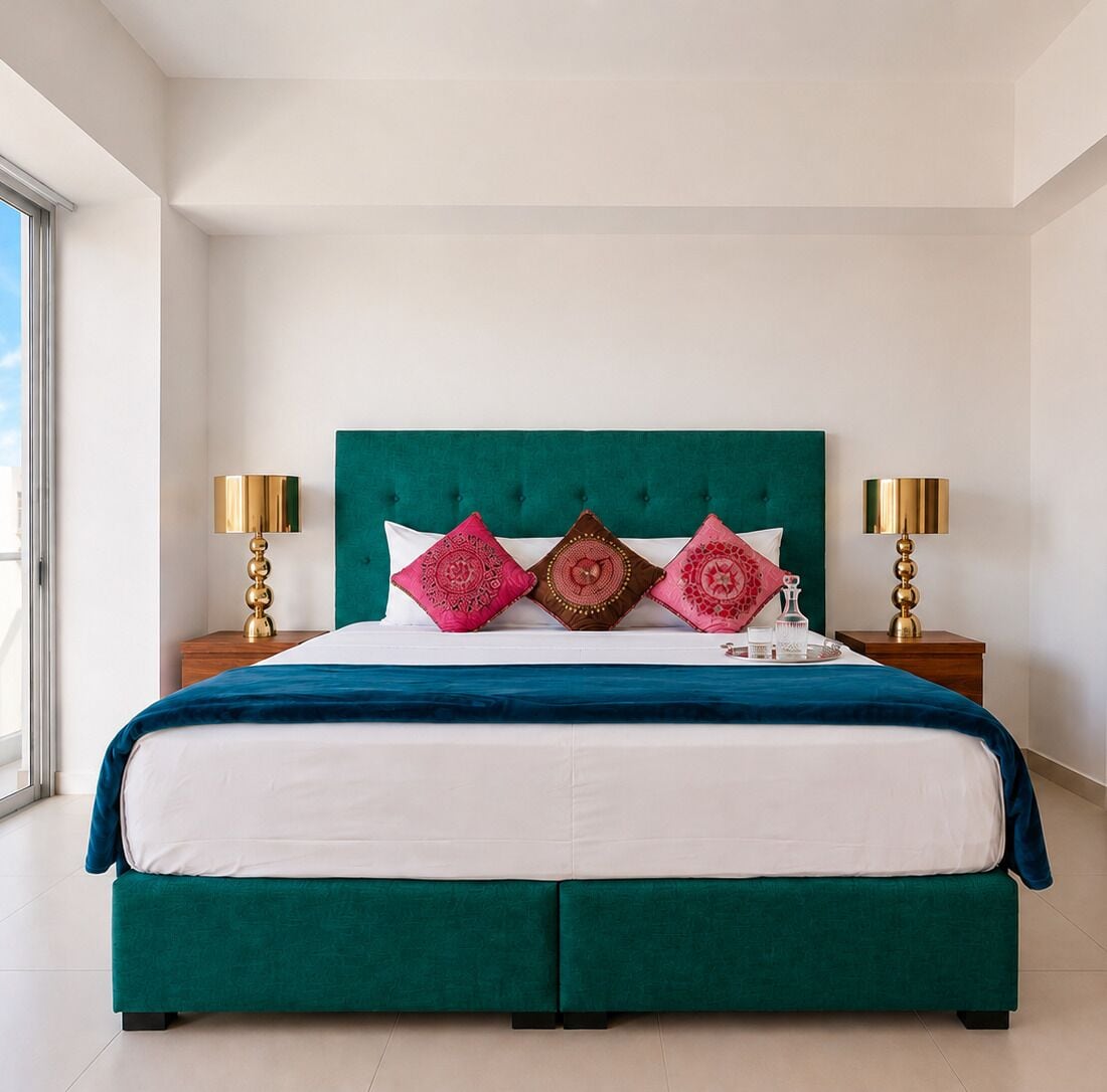 A bed with a teal headboard, white bedding, and decorative pillows. There are two bedside tables with lamps.