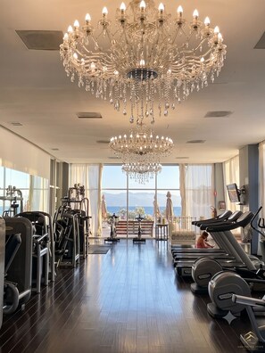 A gym with exercise equipment, a large chandelier, and a view of the sea.