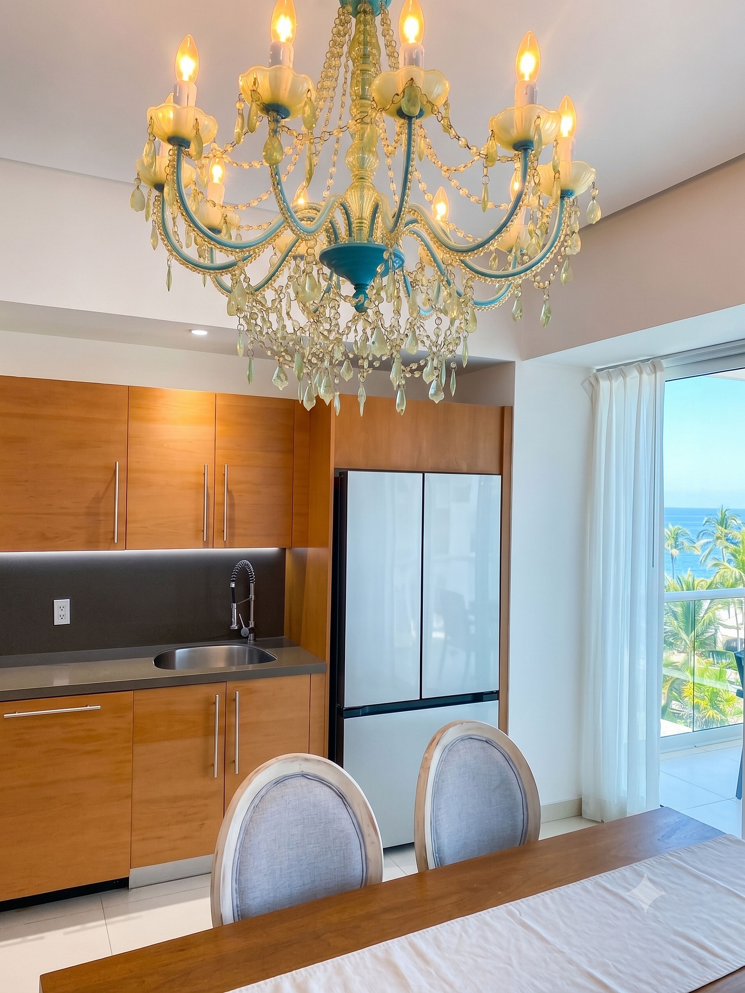 A modern kitchen with wooden cabinets, a stainless steel sink, and a large window with a view of palm trees.