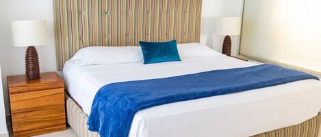 A hotel room with a striped headboard, a bed with a blue blanket, white bedding, and two bedside lamps.