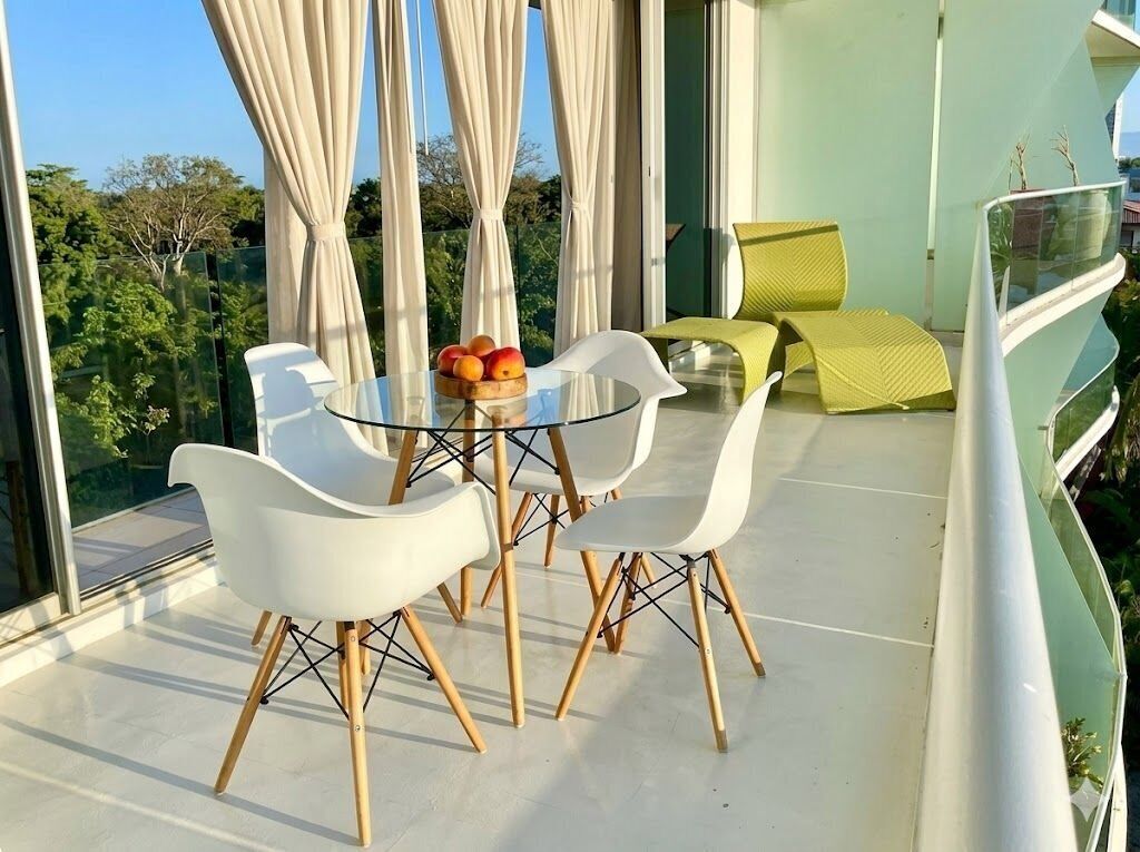 A balcony with a glass table, white chairs, and a fruit bowl.