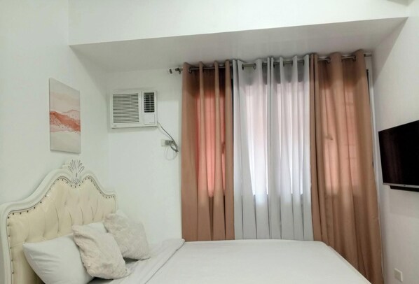 A bedroom with a bed, a headboard, a wall-mounted air conditioner, a window with curtains, and a flat-screen TV. - Grand Riviera Neas Slec (Manila)