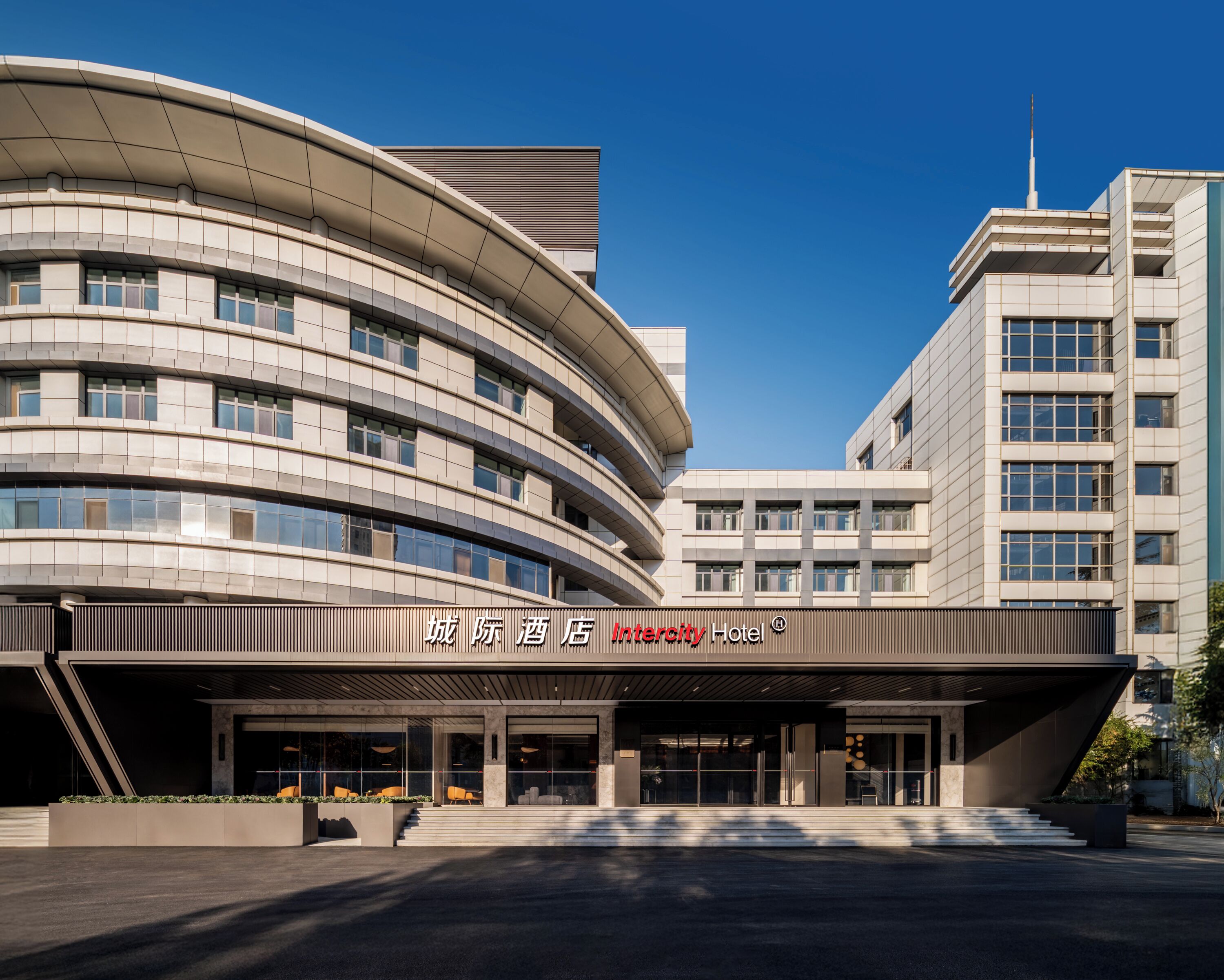 A modern hotel with a curved facade, large windows, and a prominent entrance.