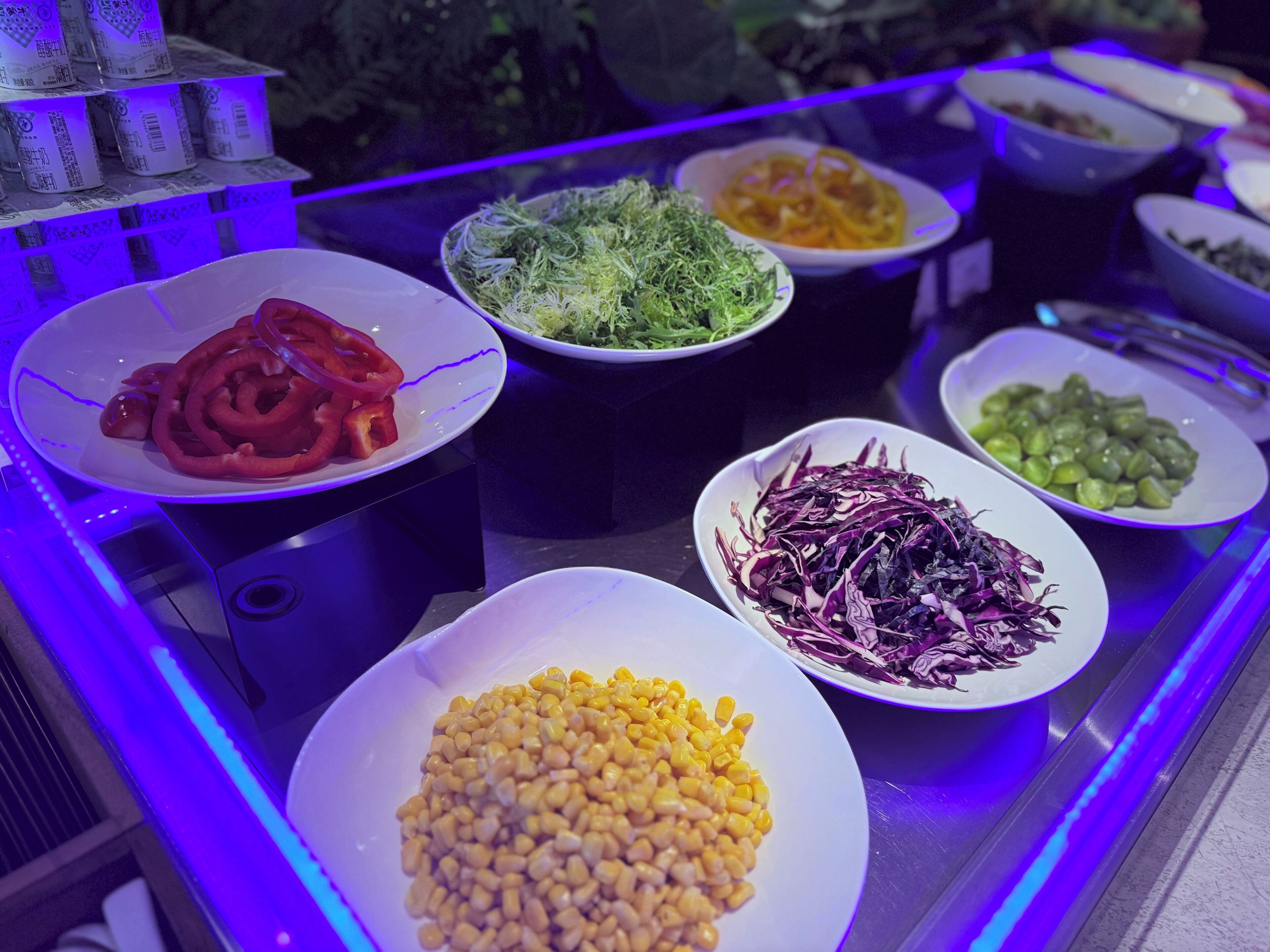A buffet with various dishes including corn, red peppers, and mixed greens.