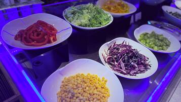 A buffet with various dishes including corn, red peppers, and mixed greens.
