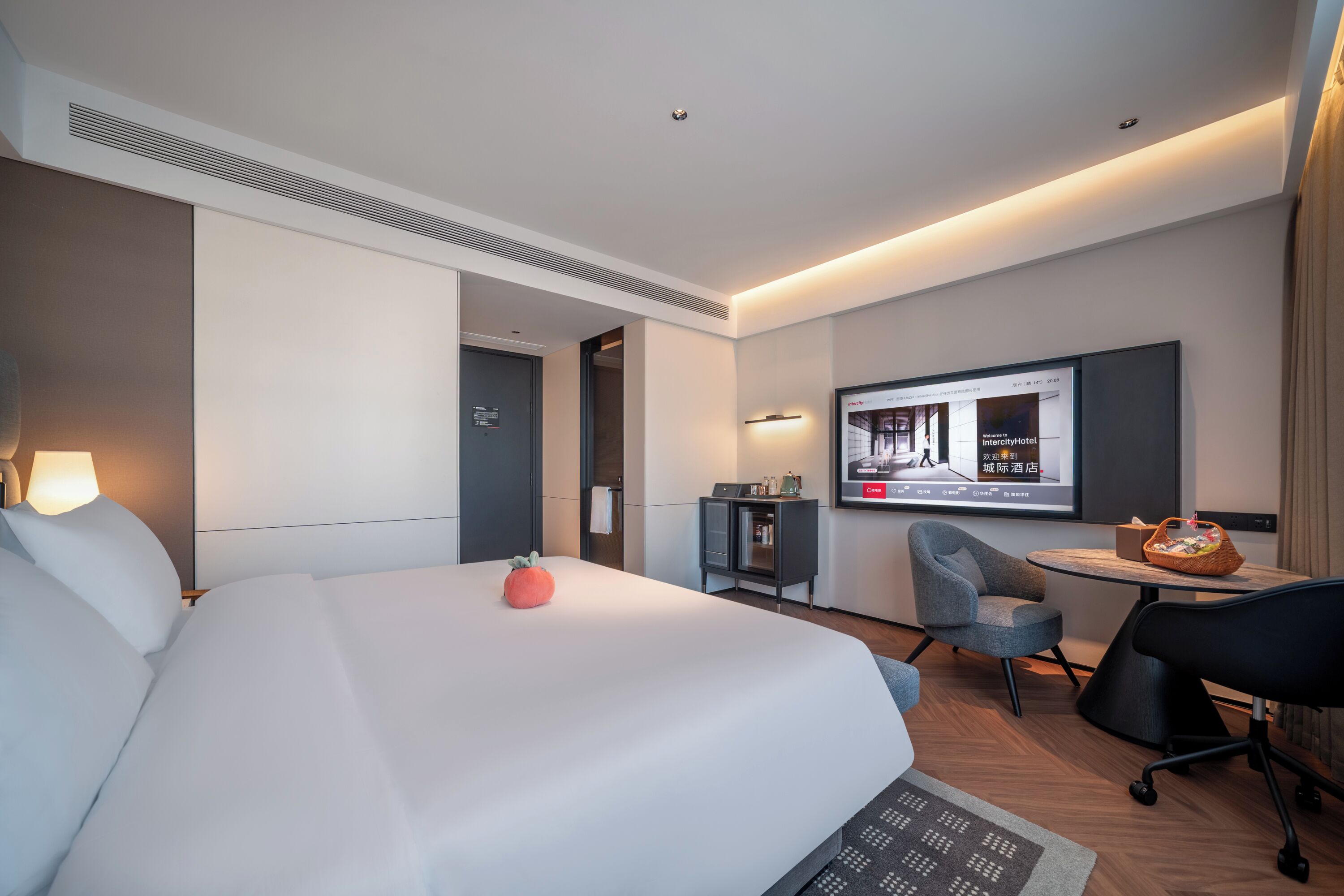 Ein Hotelzimmer mit einem Bett, einem Schreibtisch, einem Stuhl, einem Fernseher und einem kleinen Tisch mit einem Korb.
