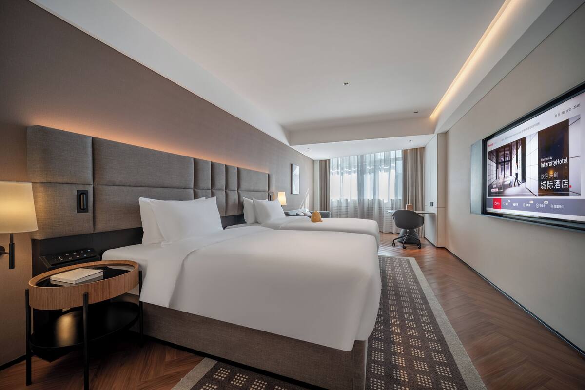 Una habitación de hotel moderna con una cama grande, mesitas de noche, televisión y vistas a la ciudad.