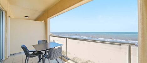 Ein Balkon mit Tisch und Stühlen mit Blick auf Strand und Meer.
