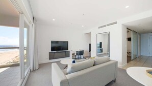 A modern living room with a sofa, TV, and dining area, large windows with a beach view, and a minimalist design.