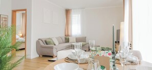 Un salon moderne avec un canapé, une table à manger dressée avec de la vaisselle et des verres, et une plante.