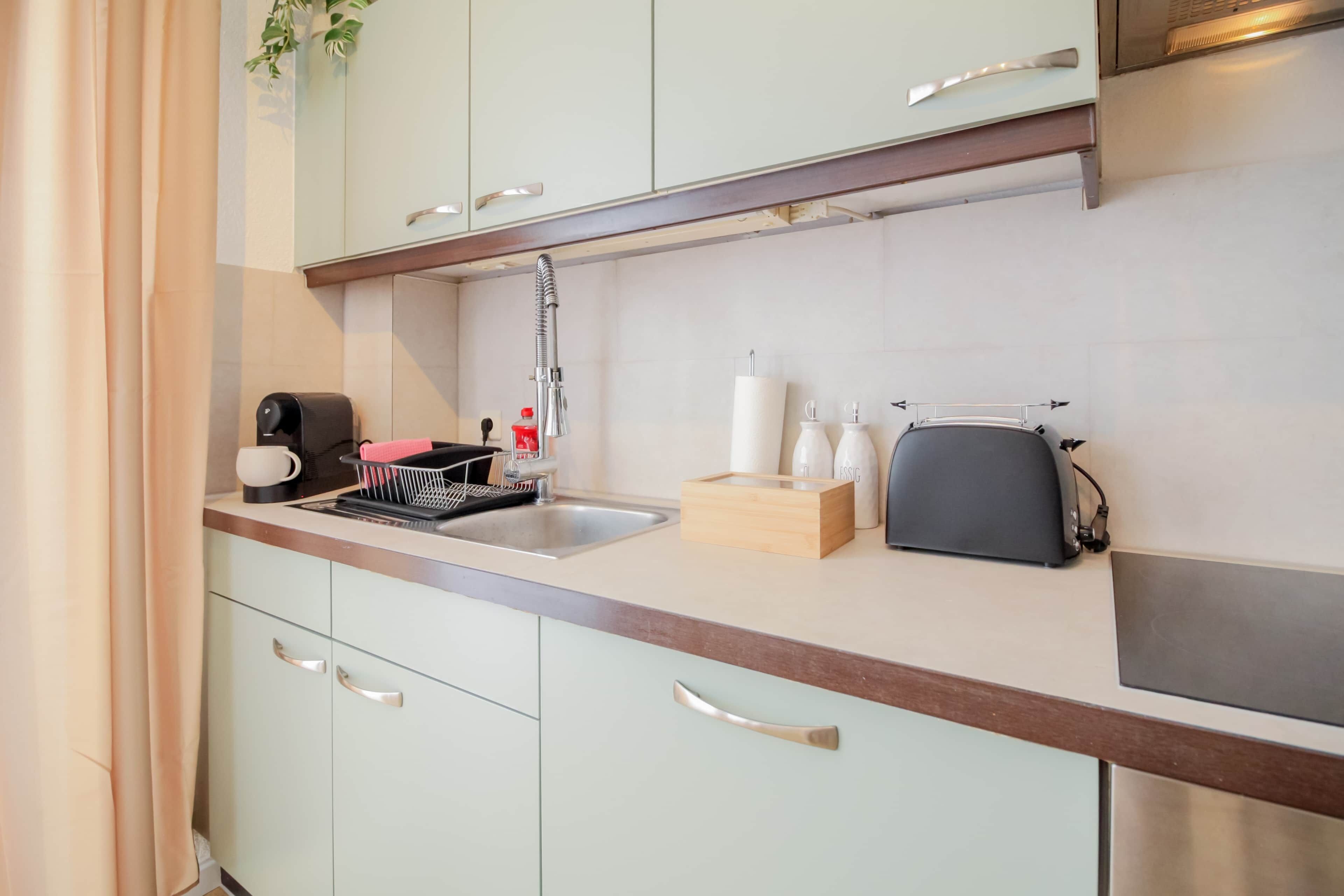 Een kitchenette met een spoelbak, een koffiezetapparaat, een waterkoker en een klein aanrecht.