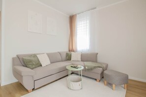 Un salon moderne avec un canapé beige, une petite table ronde, un pouf gris et un tapis blanc.
