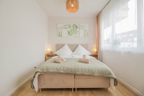 Une chambre à coucher avec un lit, des lampes de chevet, une fenêtre avec des rideaux et des œuvres d’art murales.