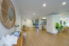 A spacious living area with a wooden floor, a round mirror, a dining table with chairs, and a kitchen area with cabinets and a sink. - Endless Summer Stay, Noosa Heads (Noosa Heads)
